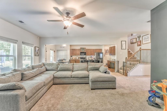 carpeted living area featuring ceiling fan and stairway