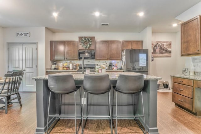 kitchen with black microwave, decorative backsplash, a kitchen bar, and a kitchen island with sink