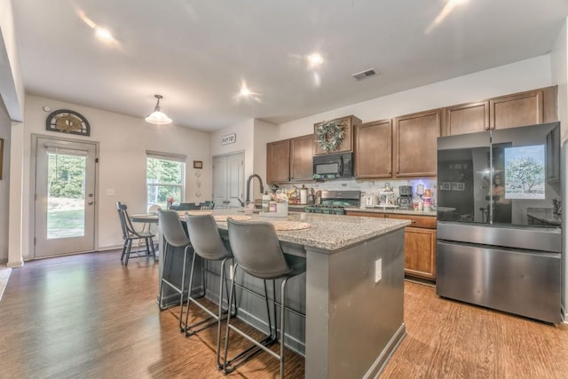 kitchen with smart refrigerator, black microwave, stove, a kitchen island with sink, and wood finished floors
