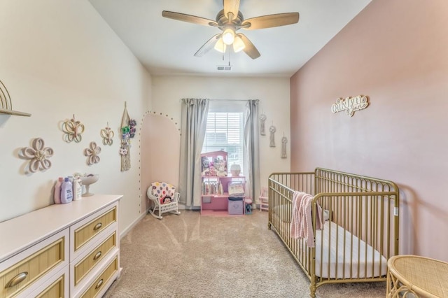 bedroom featuring a crib, light colored carpet, and a ceiling fan