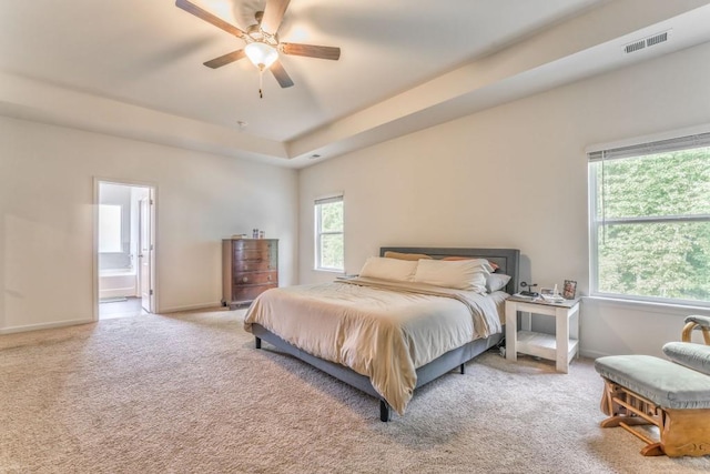 carpeted bedroom with connected bathroom, a raised ceiling, baseboards, and a ceiling fan