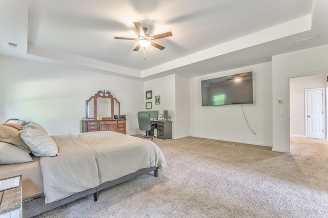 carpeted bedroom with a raised ceiling, baseboards, a desk, and ceiling fan