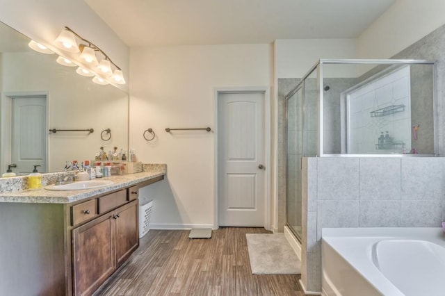 bathroom with wood finished floors, a shower stall, vanity, a bath, and baseboards