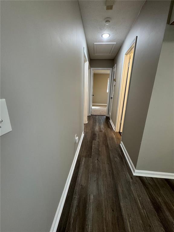 corridor with a textured ceiling and dark wood-type flooring