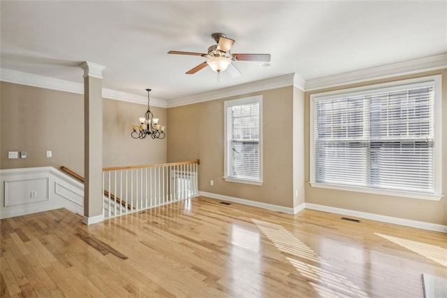 spare room featuring ceiling fan with notable chandelier, wood-type flooring, ornamental molding, and decorative columns