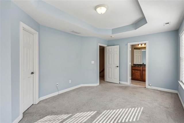 unfurnished bedroom featuring a raised ceiling, light colored carpet, and ensuite bath