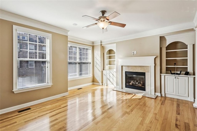 unfurnished living room featuring light hardwood / wood-style flooring, built in shelves, ceiling fan, a premium fireplace, and ornamental molding