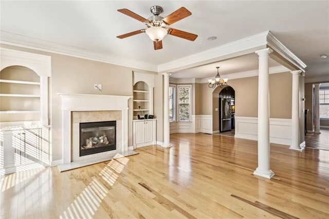 unfurnished living room with built in shelves, a high end fireplace, crown molding, ceiling fan with notable chandelier, and hardwood / wood-style flooring