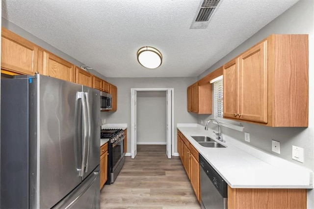 kitchen with light hardwood / wood-style flooring, stainless steel appliances, a textured ceiling, and sink