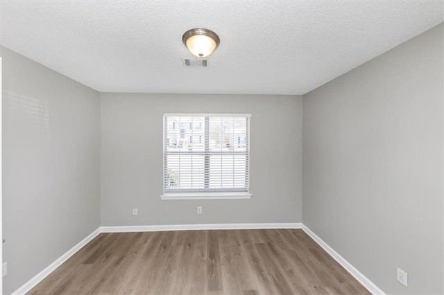 empty room with light wood-type flooring and a textured ceiling