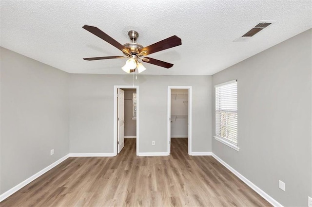 unfurnished bedroom featuring a closet, a walk in closet, light wood-type flooring, a textured ceiling, and ceiling fan