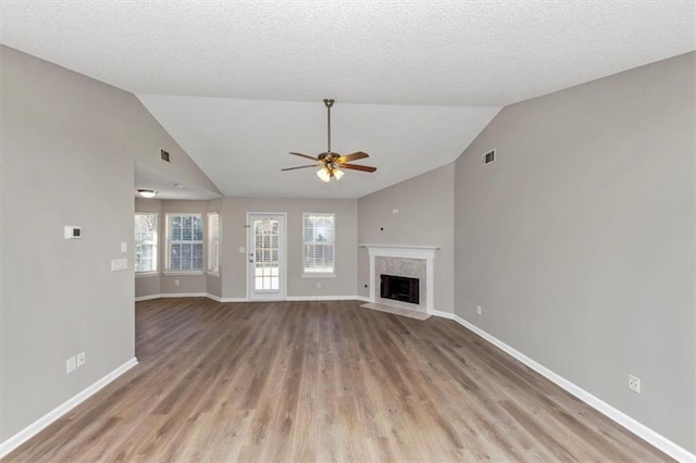 unfurnished living room featuring a high end fireplace, a textured ceiling, lofted ceiling, ceiling fan, and light wood-type flooring