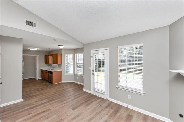 unfurnished living room featuring sink, vaulted ceiling, a textured ceiling, and light hardwood / wood-style floors