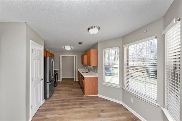 kitchen with light wood-type flooring, sink, stainless steel fridge, and a textured ceiling