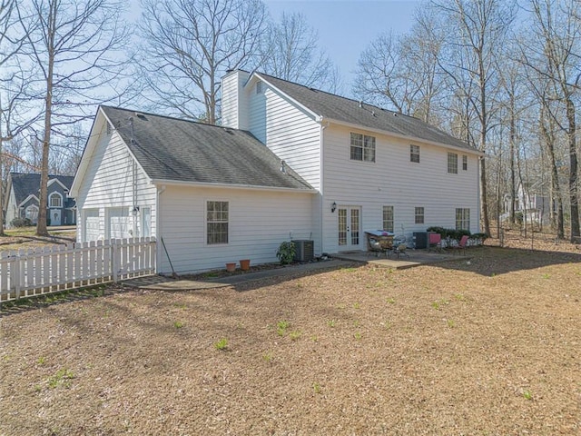 rear view of property with a shingled roof, cooling unit, french doors, a chimney, and a garage