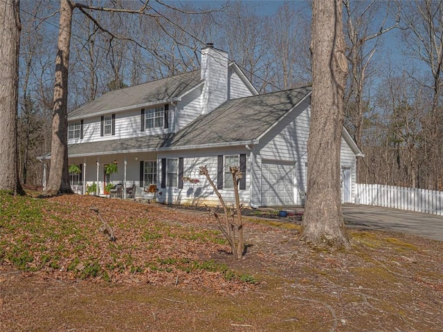 view of front of house with fence, covered porch, a chimney, a garage, and driveway