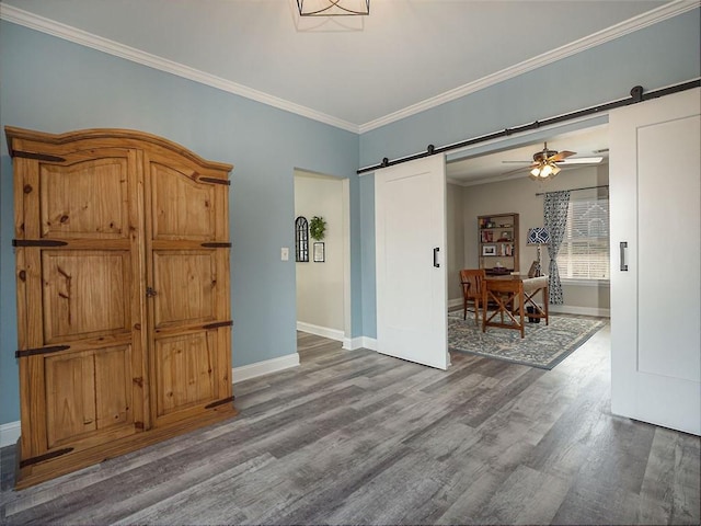 empty room with crown molding, ceiling fan, baseboards, a barn door, and wood finished floors