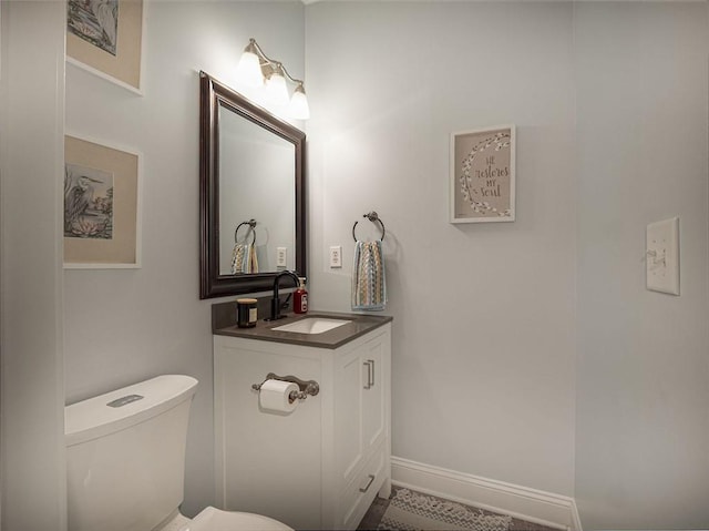 half bath featuring vanity, toilet, and baseboards