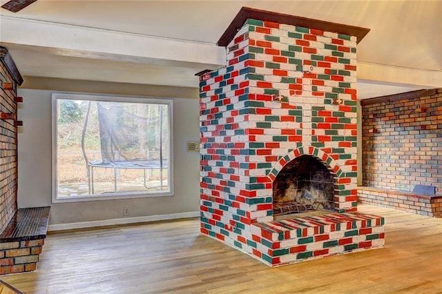 living room featuring a fireplace, beamed ceiling, wood-type flooring, and brick wall