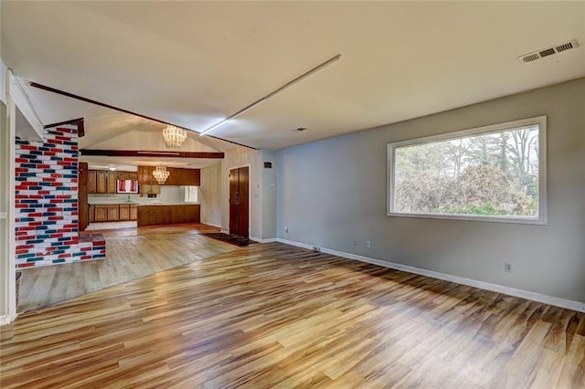 unfurnished living room featuring lofted ceiling, light wood-type flooring, and a chandelier