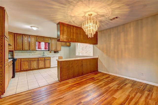 kitchen with white dishwasher, sink, hanging light fixtures, light hardwood / wood-style flooring, and a chandelier