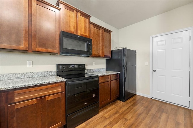 kitchen with black appliances, light hardwood / wood-style flooring, and light stone counters