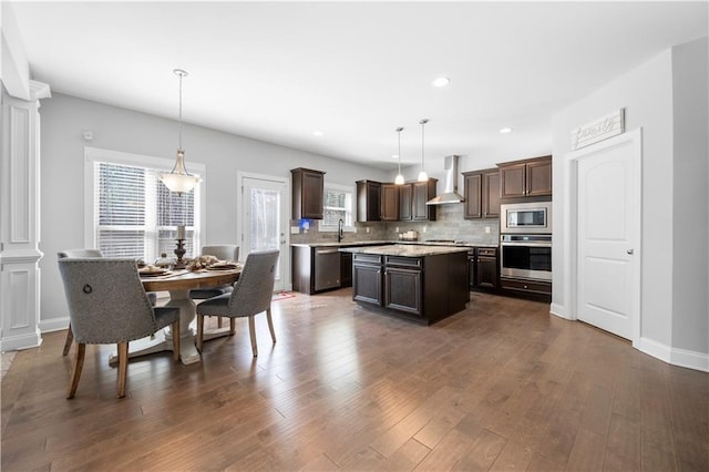 kitchen featuring pendant lighting, stainless steel appliances, a kitchen island, and wall chimney range hood