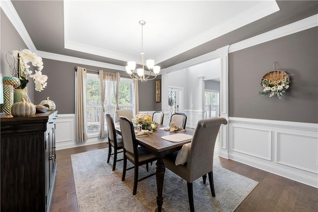 dining room with ornamental molding, dark wood-type flooring, a notable chandelier, and a tray ceiling