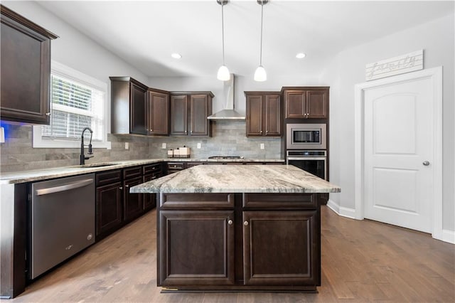 kitchen featuring hanging light fixtures, stainless steel appliances, a center island, dark brown cabinetry, and wall chimney exhaust hood