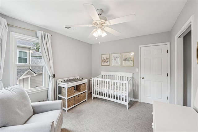 carpeted bedroom featuring a crib and ceiling fan