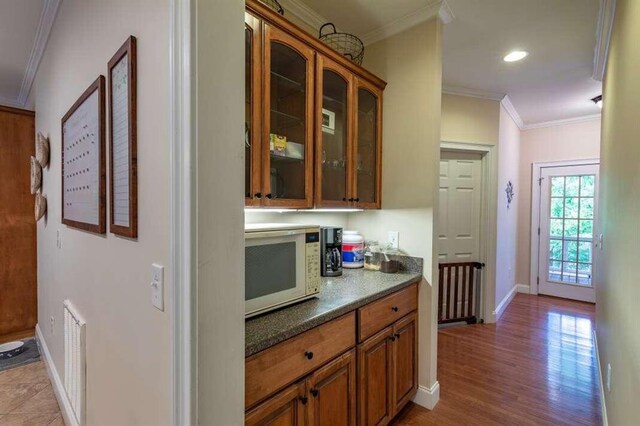 kitchen with light wood-type flooring, dark stone countertops, and crown molding