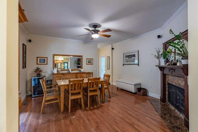 dining room featuring ornamental molding, ceiling fan, a premium fireplace, and hardwood / wood-style flooring