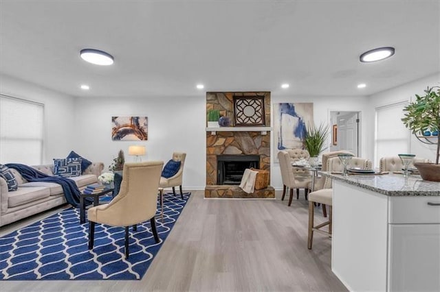 living area featuring wood finished floors, a stone fireplace, recessed lighting, and baseboards