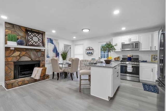 kitchen featuring appliances with stainless steel finishes, light wood-type flooring, a center island, white cabinetry, and light stone counters