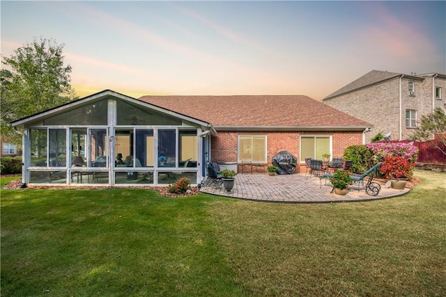 rear view of property featuring a sunroom, brick siding, a patio, and a lawn