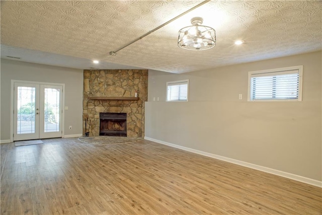 unfurnished living room with wood finished floors, a fireplace, baseboards, recessed lighting, and french doors