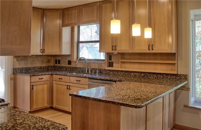 kitchen with backsplash, stainless steel dishwasher, a sink, dark stone countertops, and a peninsula