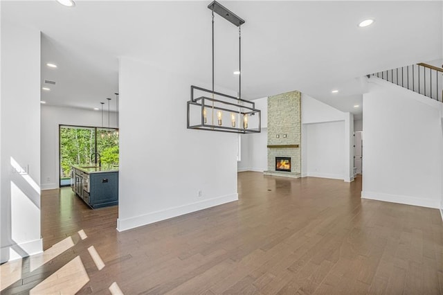 unfurnished living room with recessed lighting, stairway, a stone fireplace, dark wood-type flooring, and baseboards