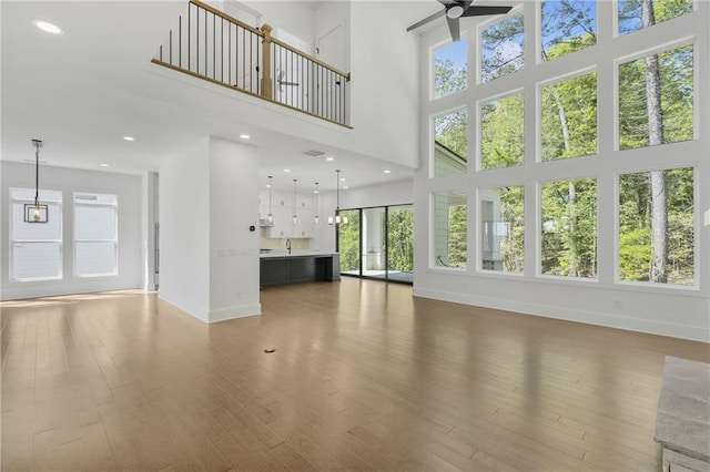 unfurnished living room featuring baseboards, a ceiling fan, wood finished floors, and a wealth of natural light