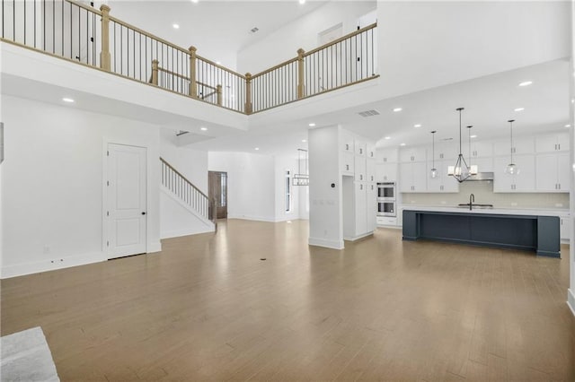 unfurnished living room featuring a sink, wood finished floors, a towering ceiling, visible vents, and recessed lighting