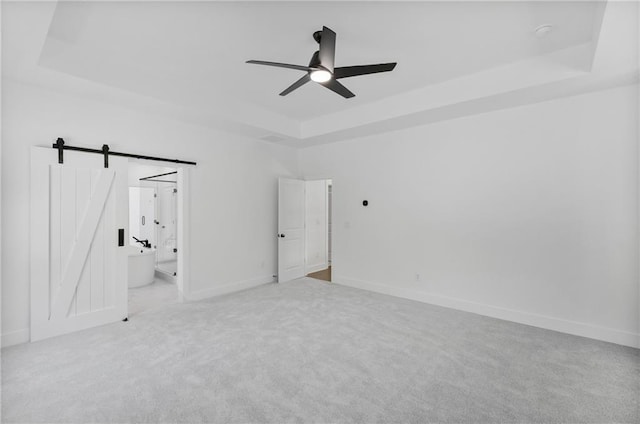 unfurnished bedroom with a tray ceiling, carpet flooring, a barn door, ensuite bathroom, and baseboards
