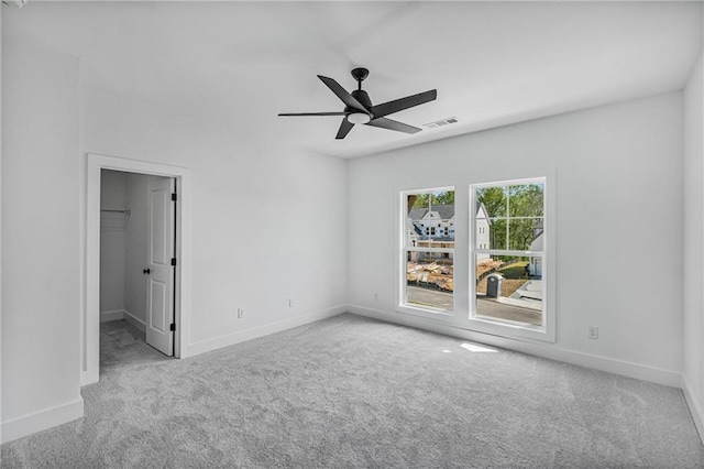 unfurnished bedroom featuring carpet, visible vents, a walk in closet, baseboards, and ceiling fan