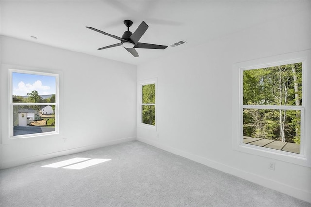 carpeted empty room with plenty of natural light, visible vents, a ceiling fan, and baseboards