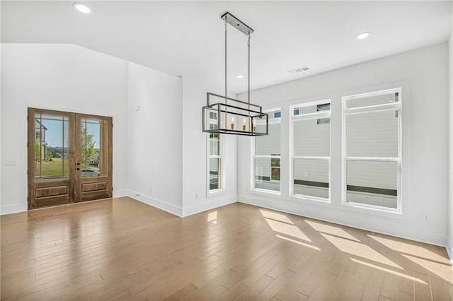 unfurnished dining area featuring wood finished floors, baseboards, a notable chandelier, and french doors