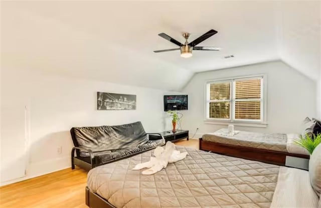 bedroom with light wood-type flooring, visible vents, vaulted ceiling, and a ceiling fan