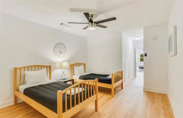 bedroom featuring a ceiling fan, light wood-style flooring, visible vents, and baseboards