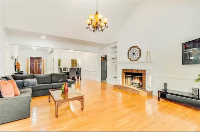 living area featuring an inviting chandelier, built in shelves, a fireplace, and wood finished floors