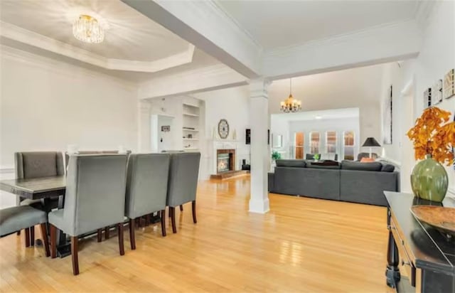 dining area with crown molding, decorative columns, light wood-style floors, a chandelier, and a lit fireplace