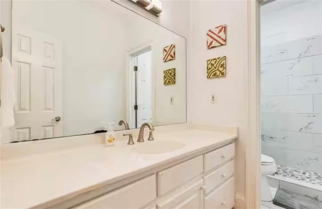 bathroom featuring toilet, a tile shower, and vanity