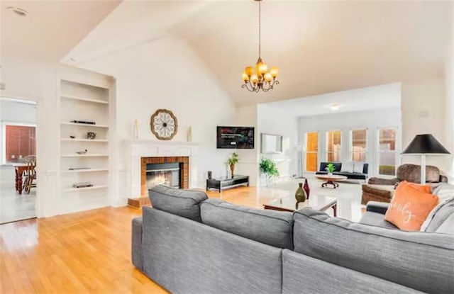 living area featuring high vaulted ceiling, a fireplace, wood finished floors, built in features, and an inviting chandelier